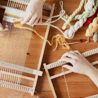 Hands of two professional crafters weaving a rug to sell for profit