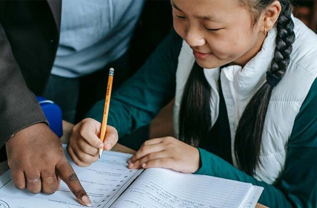Student holding a pencil and a teacher pointing to the student's workbook