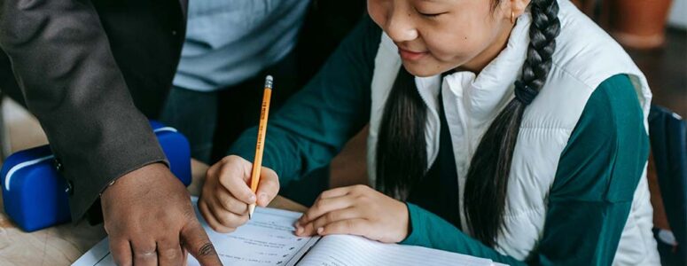 Student holding a pencil and a teacher pointing to the student's workbook