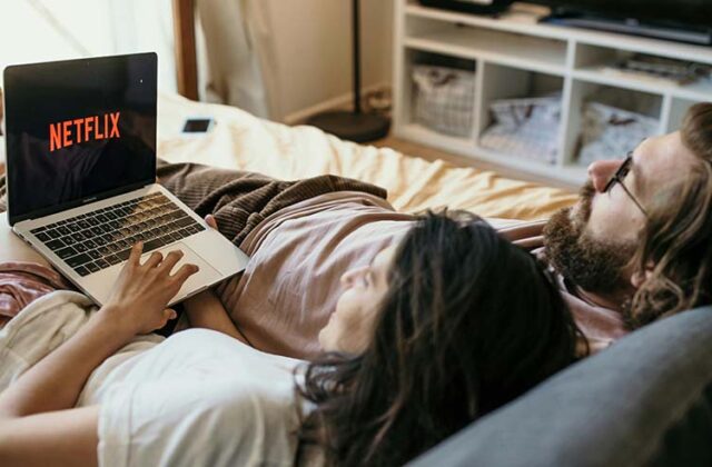 Woman lying on her bed watching Netflix on her laptop.