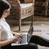 Freelance writer sitting on the floor working on a project on her laptop.