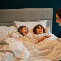 Overnight babysitter/nanny telling a bedtime story to two children who are lying in bed