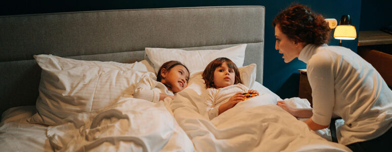 Overnight babysitter/nanny telling a bedtime story to two children who are lying in bed