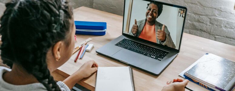 Young student at a desk with study materials and a laptop open to show an online Cambly tutor