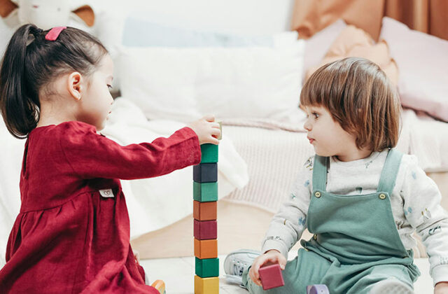 Two preschool-aged toddlers playing with colored blocks at a home daycare