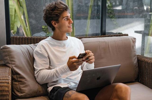 Man sitting on a couch with a laptop and phone withdrawing money from InboxDollars.