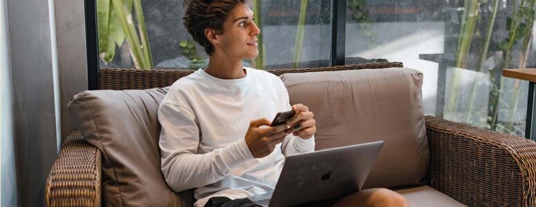 Man sitting on a couch with a laptop and phone withdrawing money from InboxDollars.