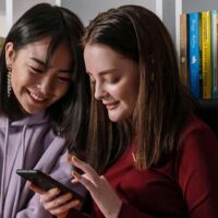 Two teenage girls taking a paid survey on a smartphone.