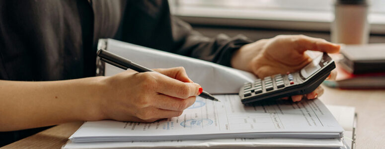 Accountant working on a calculator and taking notes for their side hustle.