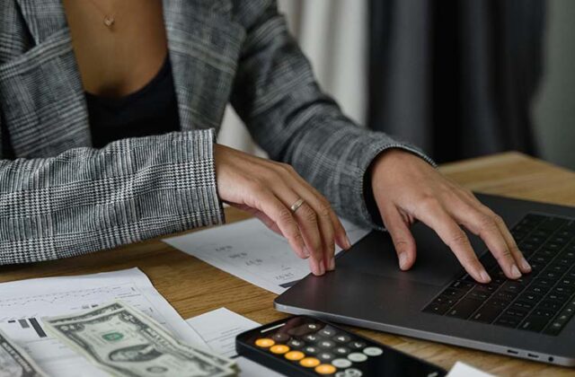 Close view of a finance professional typing on their laptop with a calculator nearby, suggesting they're working on their side hustle.