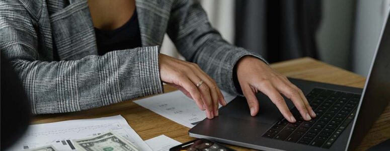 Close view of a finance professional typing on their laptop with a calculator nearby, suggesting they're working on their side hustle.