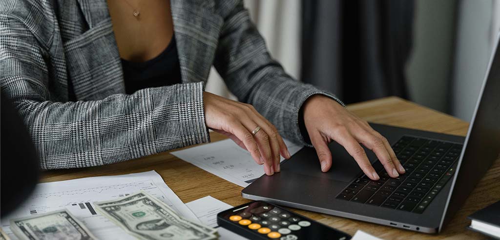 Close view of a finance professional typing on their laptop with a calculator nearby, suggesting they're working on their side hustle.