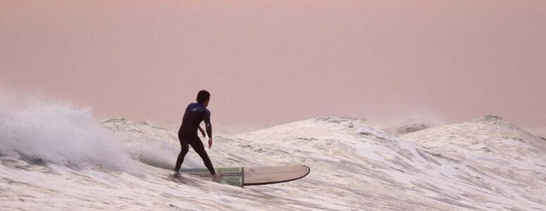 Man surfing on a break from his summer side hustle as a lifeguard.