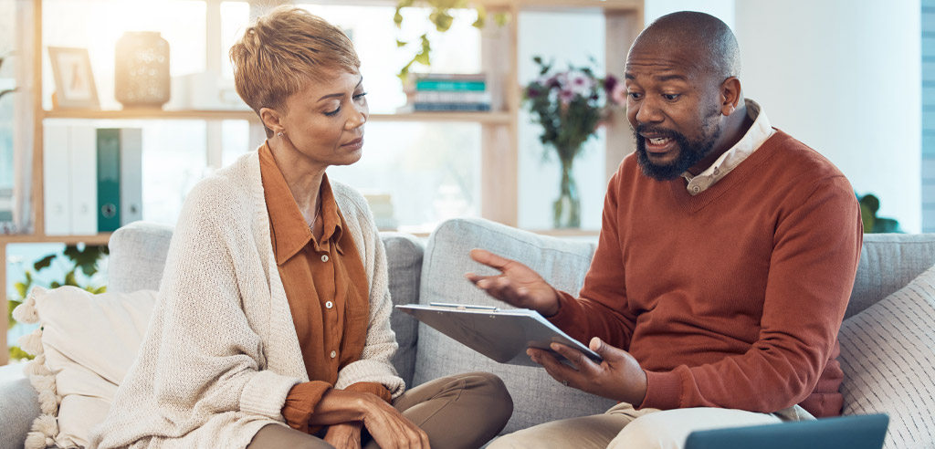 Man and woman sitting on a couch talking and reviewing their budget