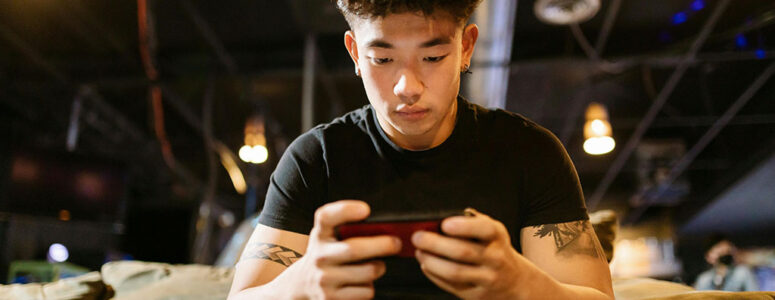 Man sitting on a couch with his smartphone using apps that pay you to sign up.