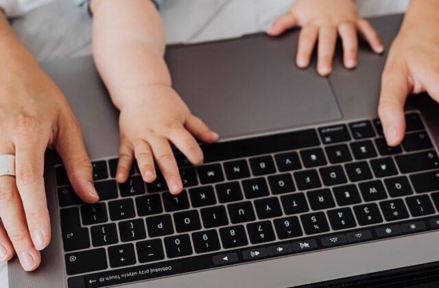 Closeup of a baby and parents' hands on a laptop keyboard.