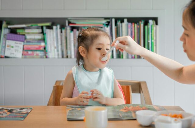 Babysitter feeding a toddler at a dining table