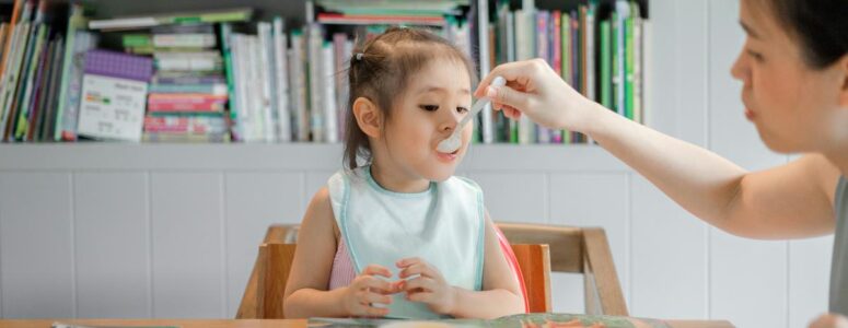 Babysitter feeding a toddler at a dining table