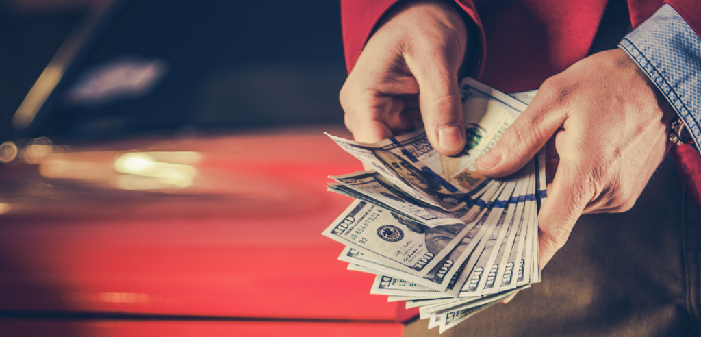 Close view of someone holding a stack of 100-dollar bills by their car