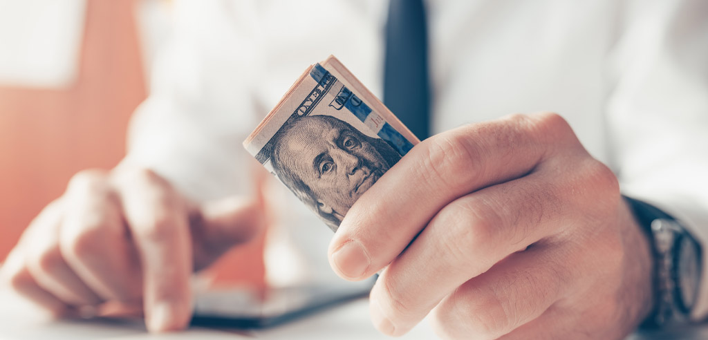 Close view of a man holding several folded hundred-dollar bills