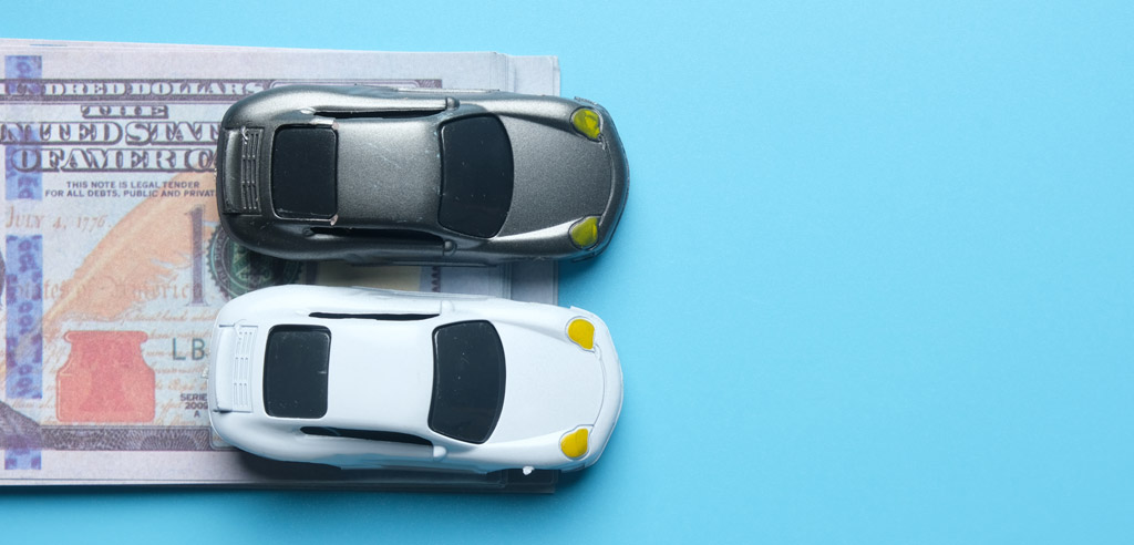 Two toy cars resting on a hundred dollar bill against a blue background