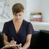 Certified coach sitting on a black couch and writing down notes for coaching clients