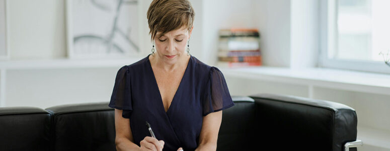 Certified coach sitting on a black couch and writing down notes for coaching clients
