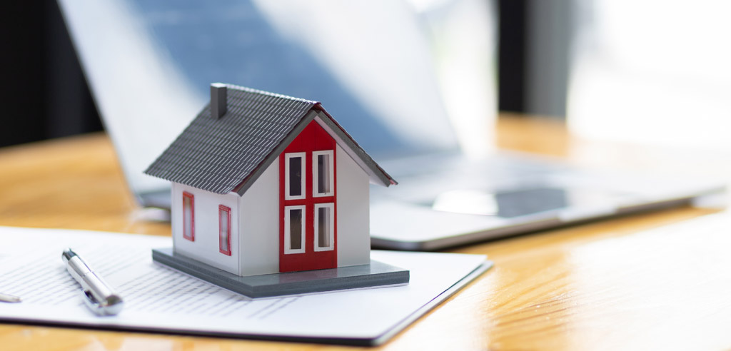 Small model of a house on top of a clipboard next to a laptop
