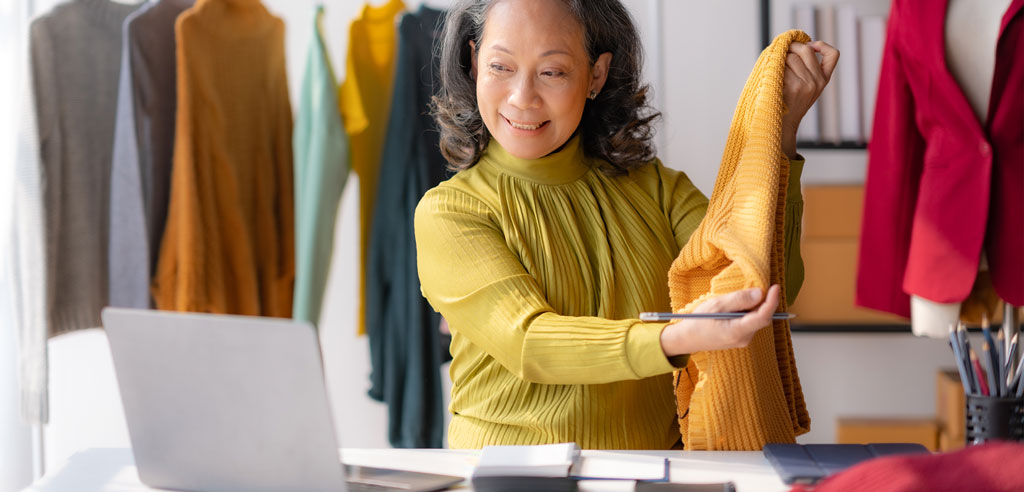 Clothing seller sitting at her laptop and handling a shirt