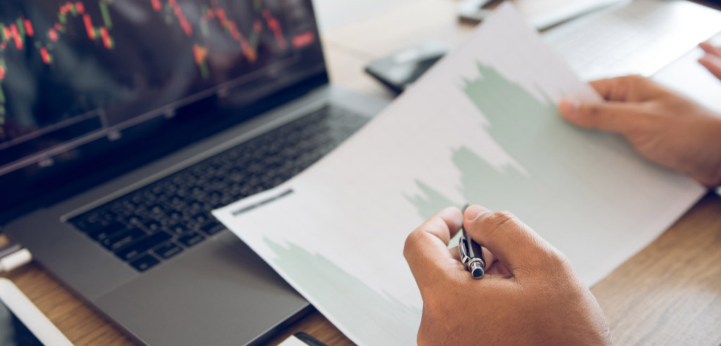 Close view of someone looking at a printout of a financial chart with candlestick diagrams on their laptop representing investing