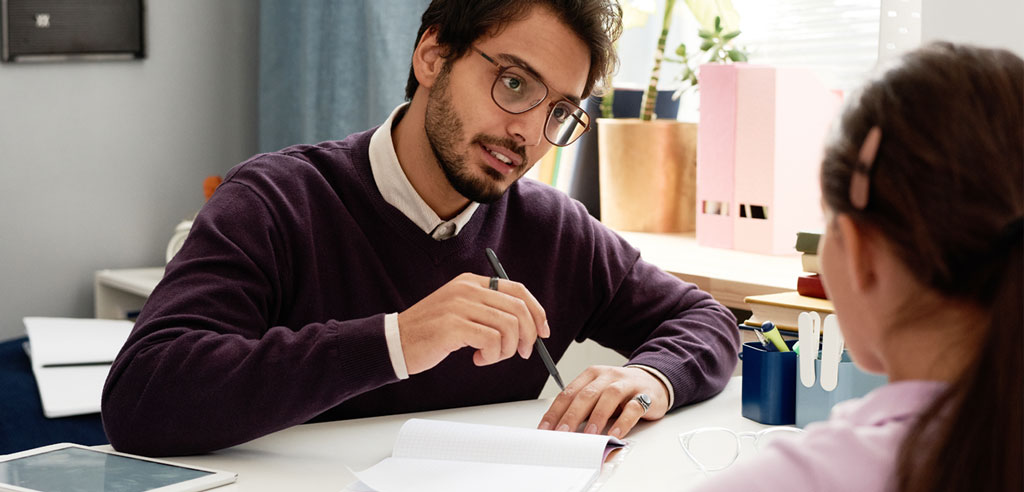Male tutor sitting at a desk and working with a female student