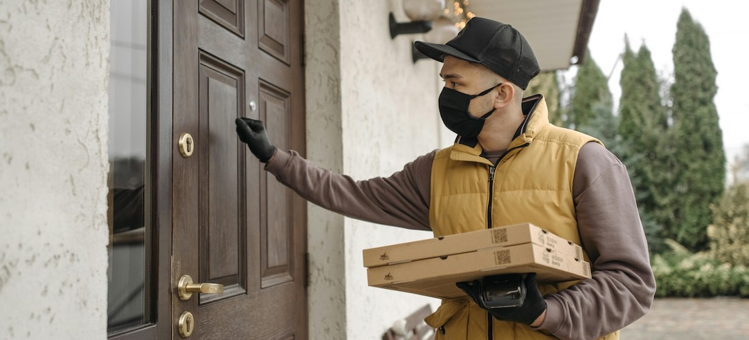 A deliveryman wearing a mask delivering pizza to a customer during the pandemic.