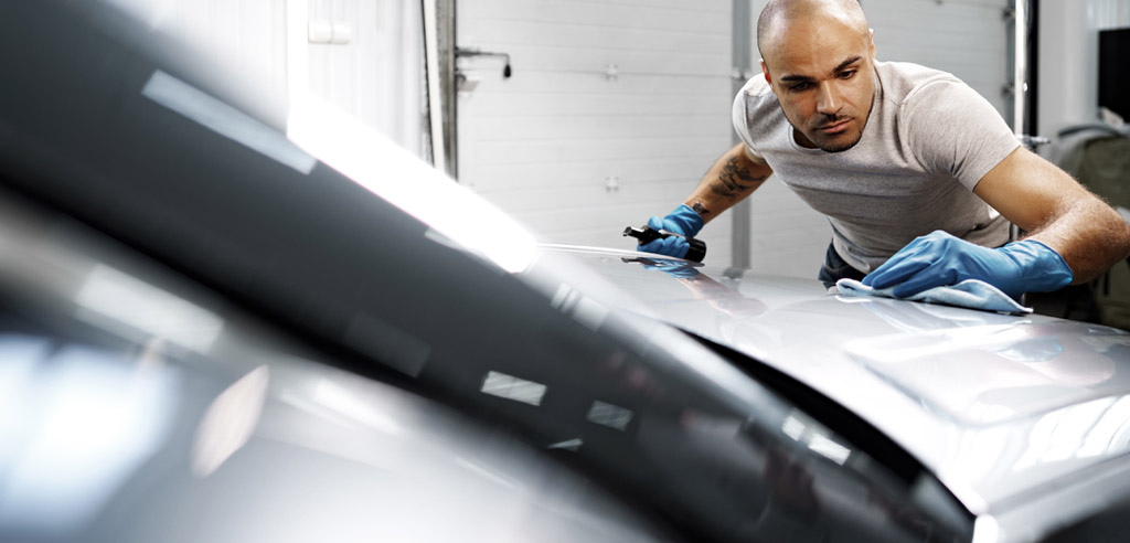 Man cleaning the outside of his car with a rag by himself to save money on his rideshare side hustle