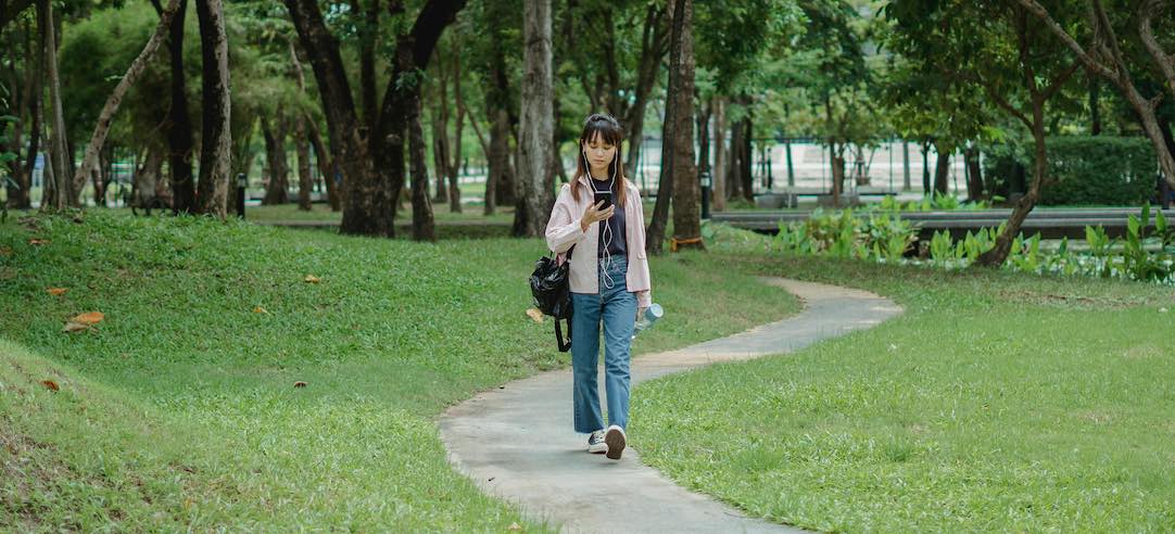 Woman walking through park while on her phone.