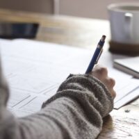 Close view of a writer at their desk holding a pen and working on an article.