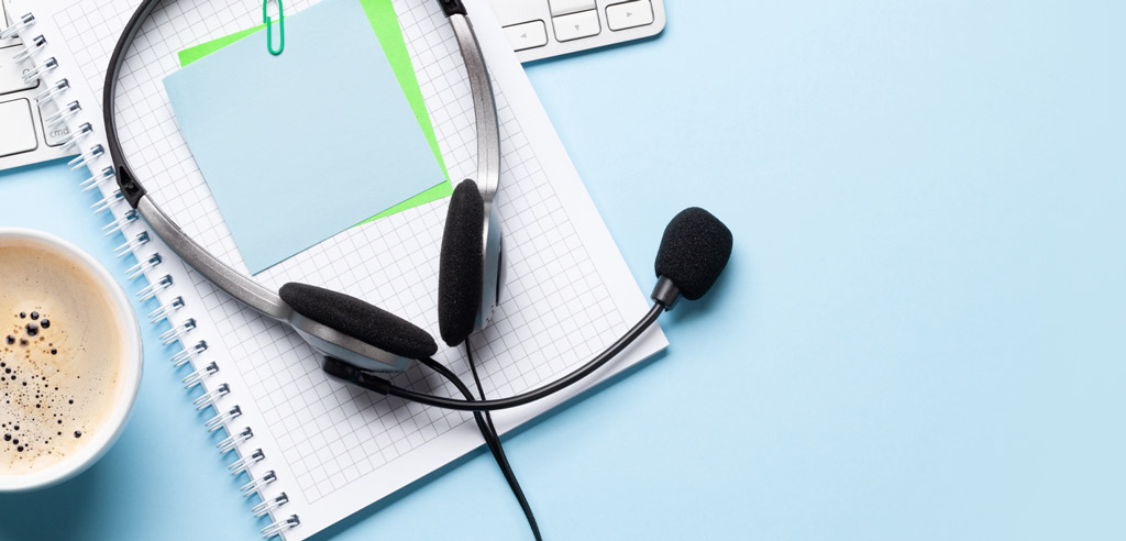 Headphones resting on a blank spiral-bound notebook next to a cup of coffee