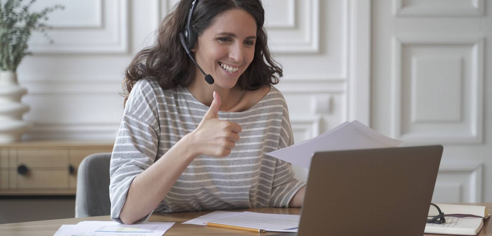 Online tutor sitting at laptop and giving a thumbs-up sign