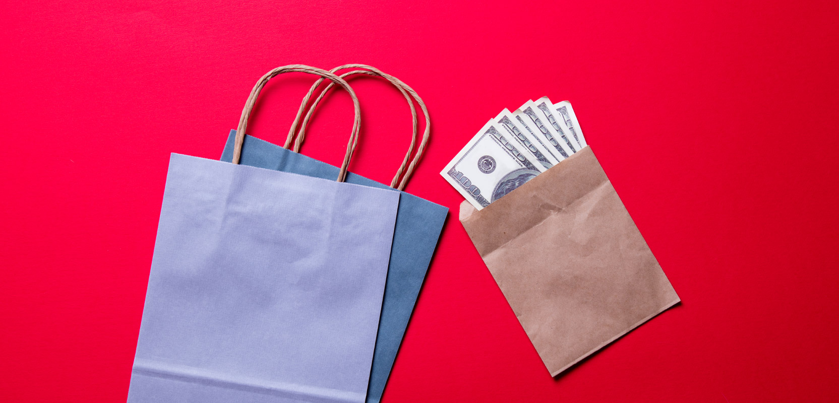 Two paper bags and an envelope with money in it against a red background, seen from the top