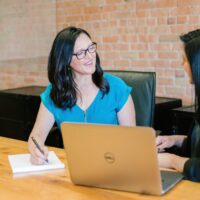 Professional consultant sitting in a meeting room with a client, with a laptop, notepad, and pen on the table
