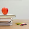 Teacher's desk with an apple, colored pencils, letter blocks, and school texts, representing the coursework that a curriculum developer creates