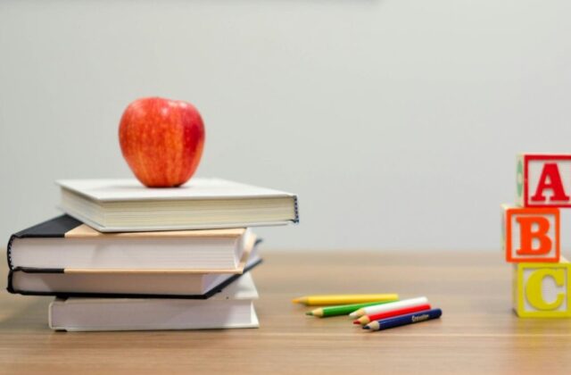 Teacher's desk with an apple, colored pencils, letter blocks, and school texts, representing the coursework that a curriculum developer creates