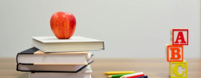 Teacher's desk with an apple, colored pencils, letter blocks, and school texts, representing the coursework that a curriculum developer creates