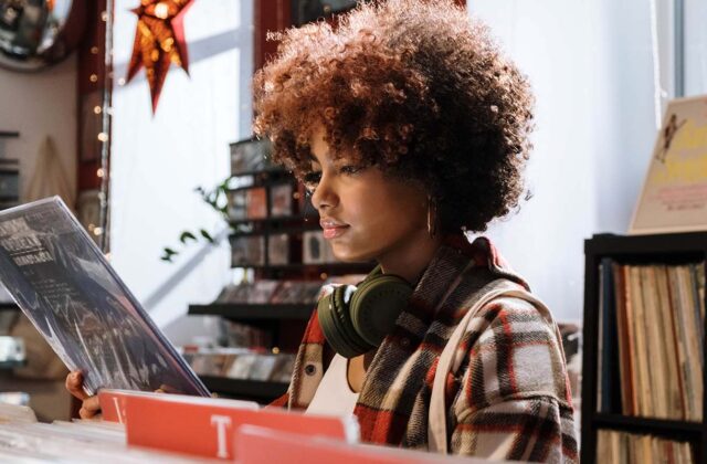 Young person in a music store, earphones around their neck, reading the back of a record