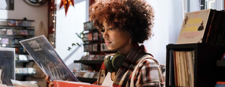 Young person in a music store, earphones around their neck, reading the back of a record