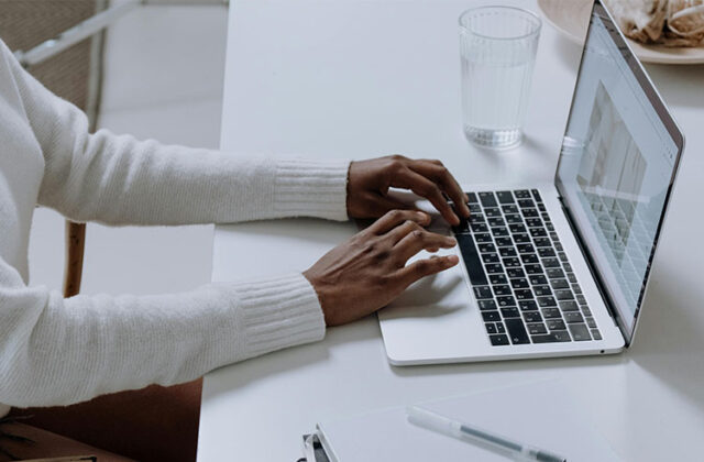 Close view of a blogger at a desk typing on their laptop