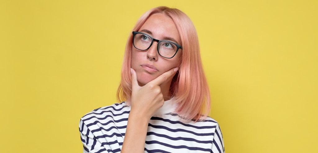 Person with pink hair and glasses looking deep in thought about whether to start a paid caregiving side hustle
