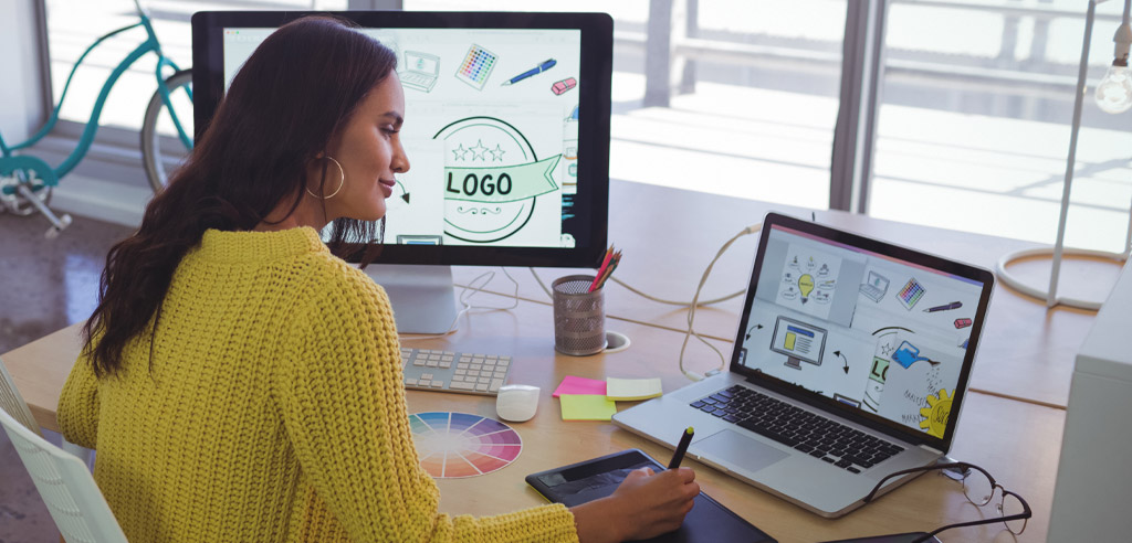 Graphic designer at her laptop drawing something on a tablet