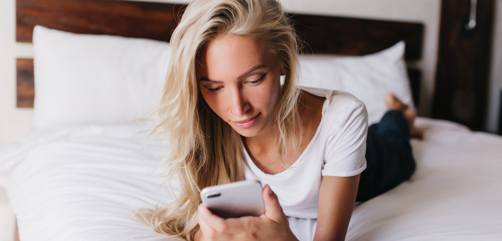 A woman laying on her bed looking down at her phone