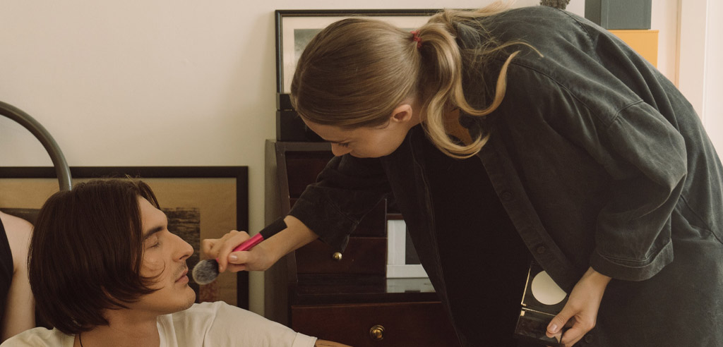 Female makeup artist applying makeup to a male client for her side hustle