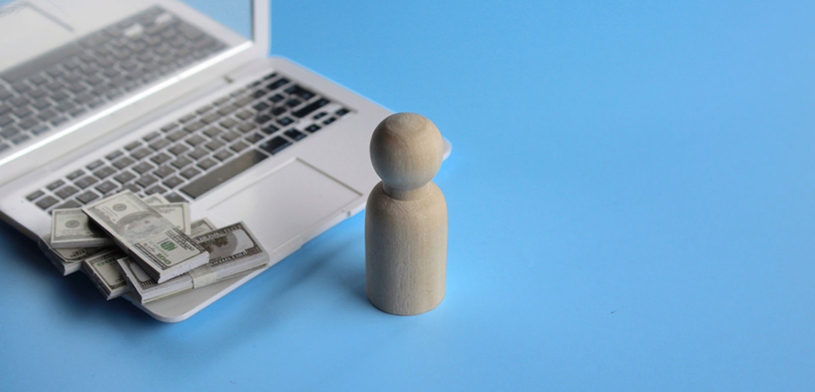 Carved wooden game piece in front of a laptop with dollar bills on the keyboard